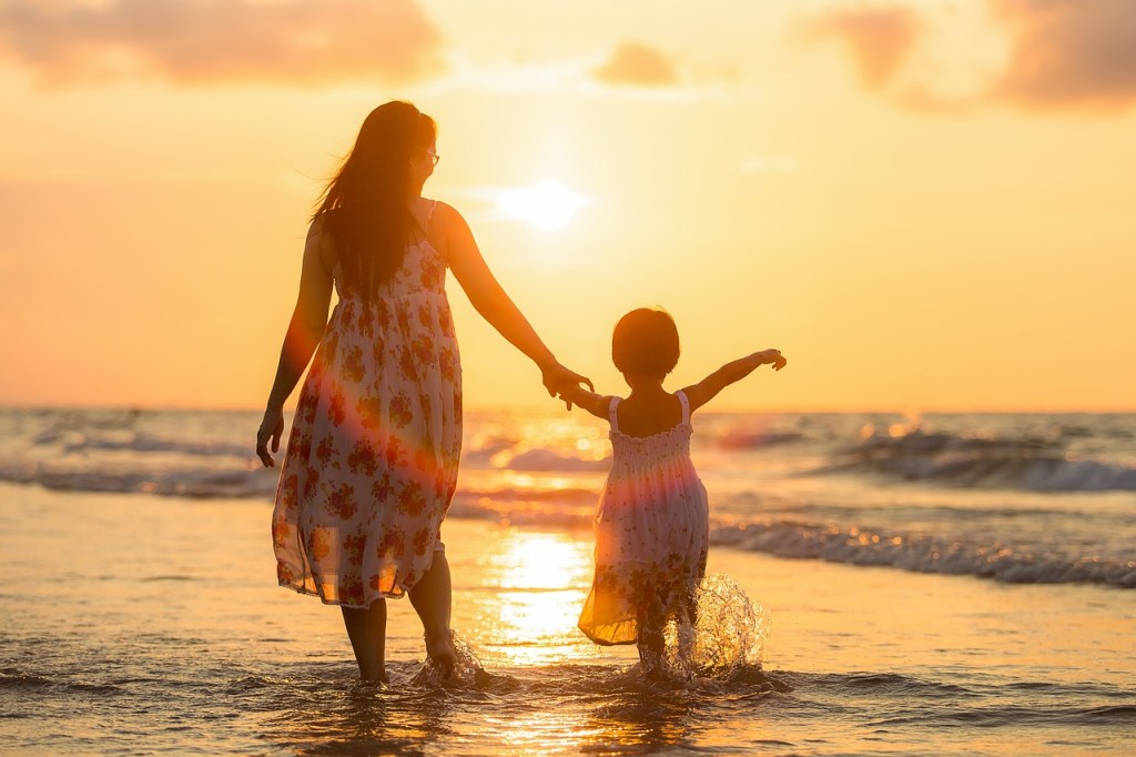 Mutter und Tochter Hand im Hand am Strand im Wasser bei Sonnenuntergang.